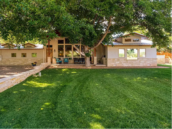 Modern house with a large tree in front, surrounded by green grass.